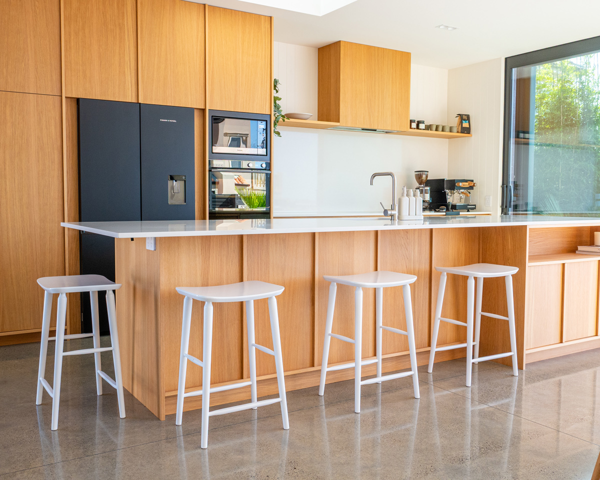 White Mackenzie bar stools styled along a modern residential kitchen island, featuring minimalist seating, oak cabinetry, and bright contemporary interiors.