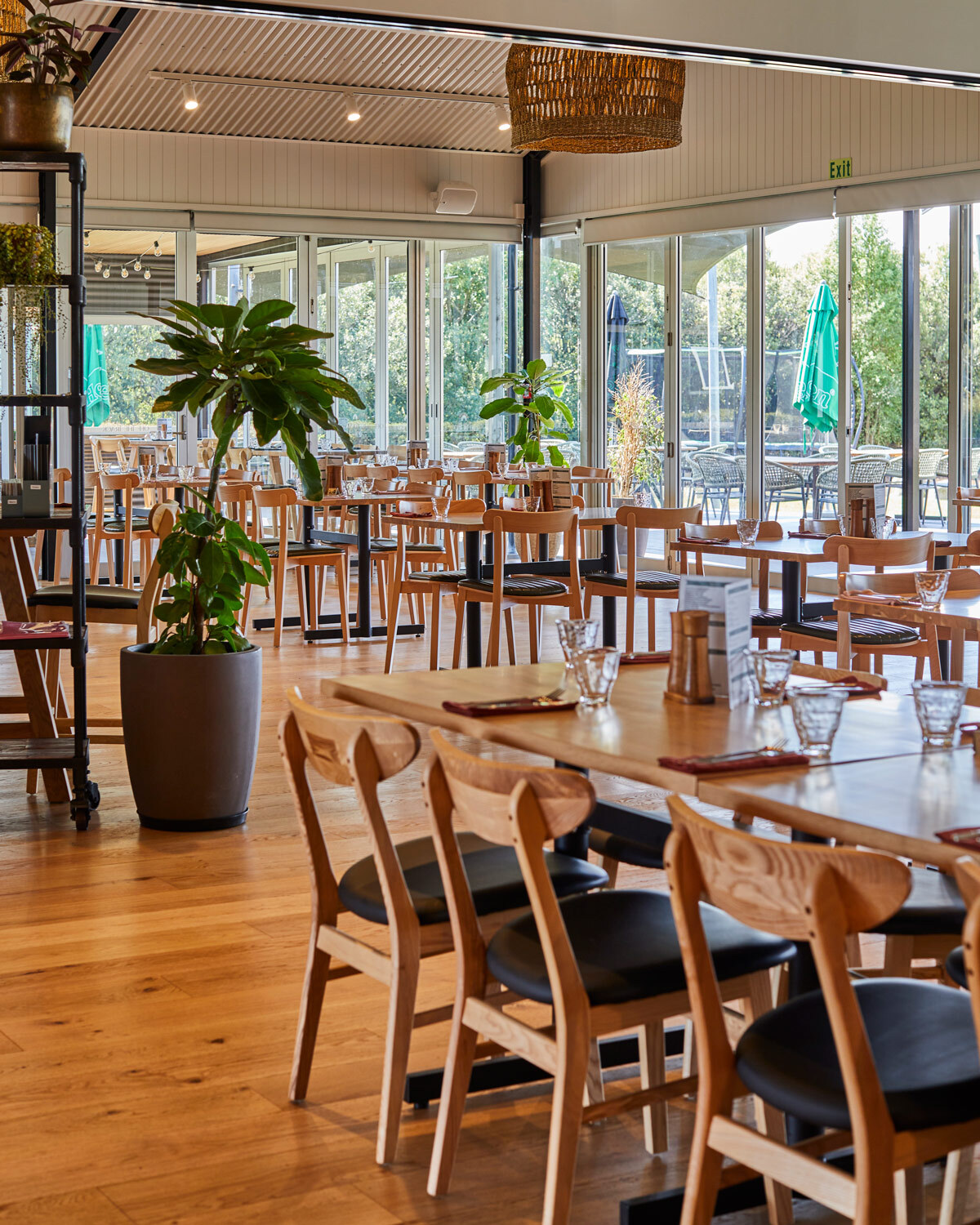 Open-plan restaurant interior showcasing timber dining tables, chairs and indoor planting throughout the space.