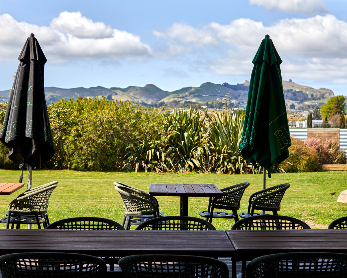 Outdoor dining area at Off The Track Restaurant with woven dining chairs and tables overlooking the Canterbury countryside.
