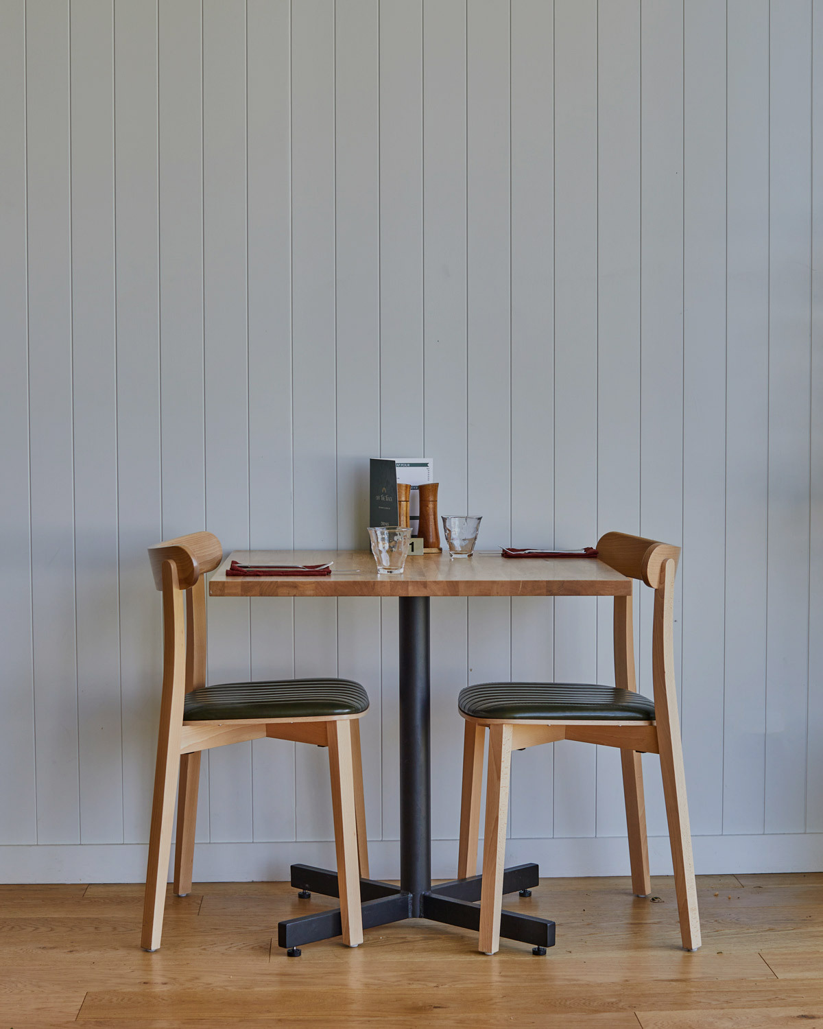 Icho dining chairs in natural paired with a black table base and timber table top sitting against a white panelled wall in a restuarant setting
