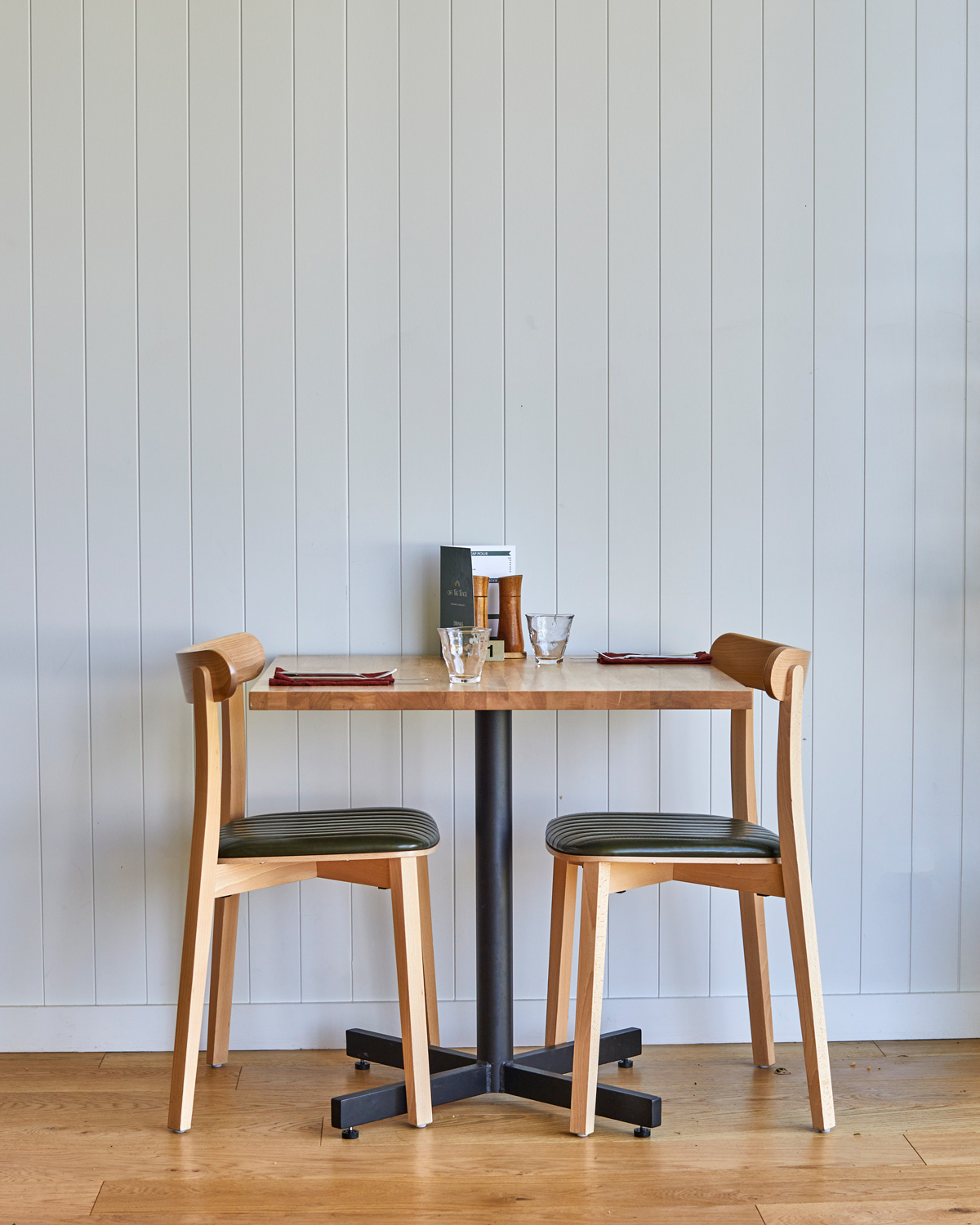 Two-seat dining setting featuring timber restaurant chairs and table in a contemporary hospitality interior.