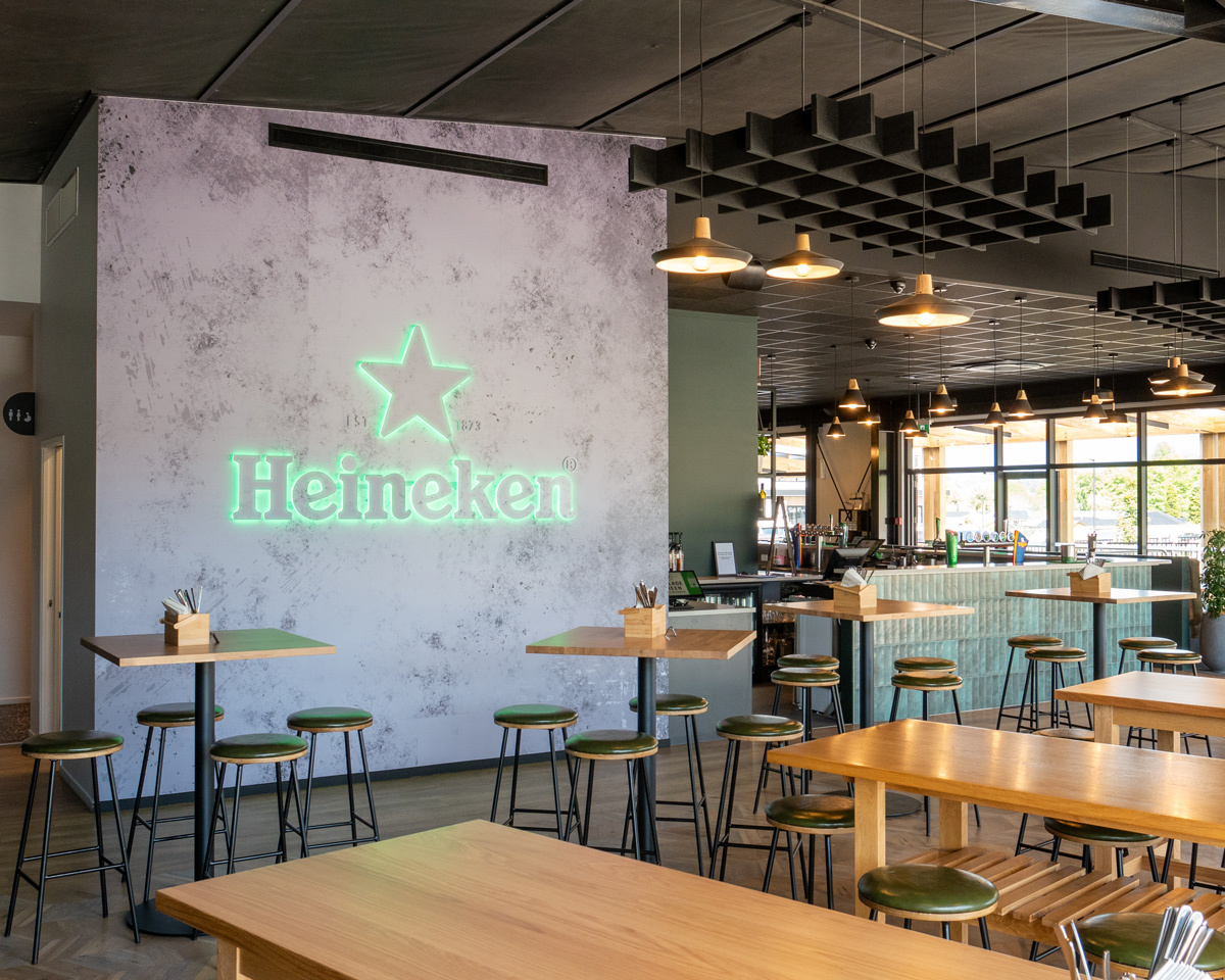 Samuel bar stools styled throughout a contemporary restaurant and bar, featuring upholstered green seats, black metal frames, and timber hospitality tables.