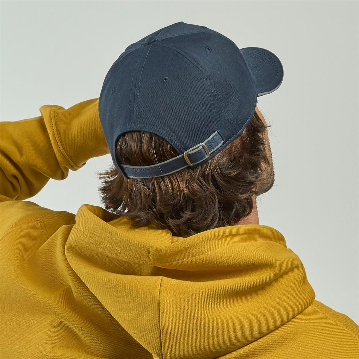 A navy cap with an adjustable strap, worn by a person in a yellow hoodie, viewed from the back.