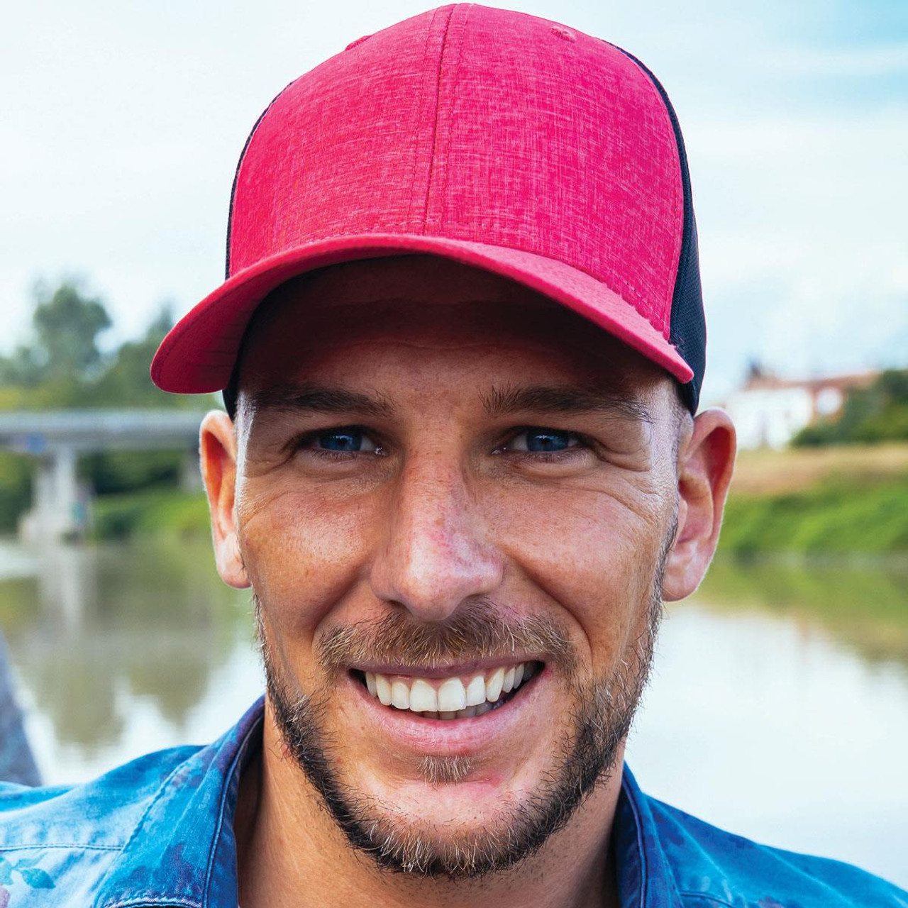 A cap featuring a red front and black mesh backing, set against a blurred outdoor background.