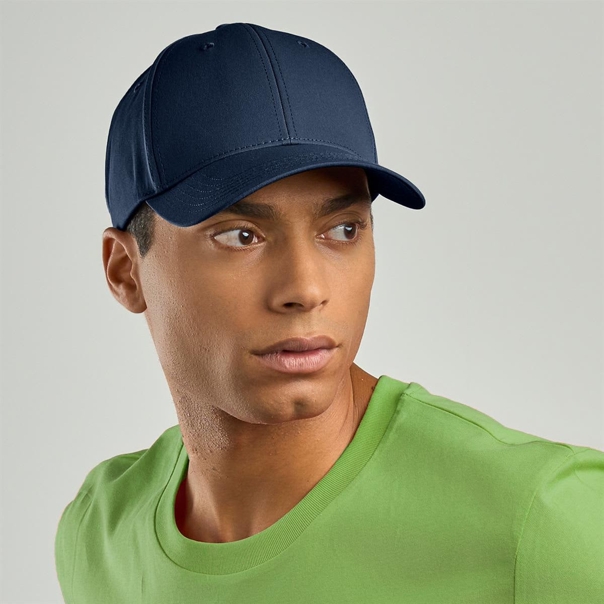 A navy cap with a structured design, worn by a model in a green T-shirt. The cap features a logo.