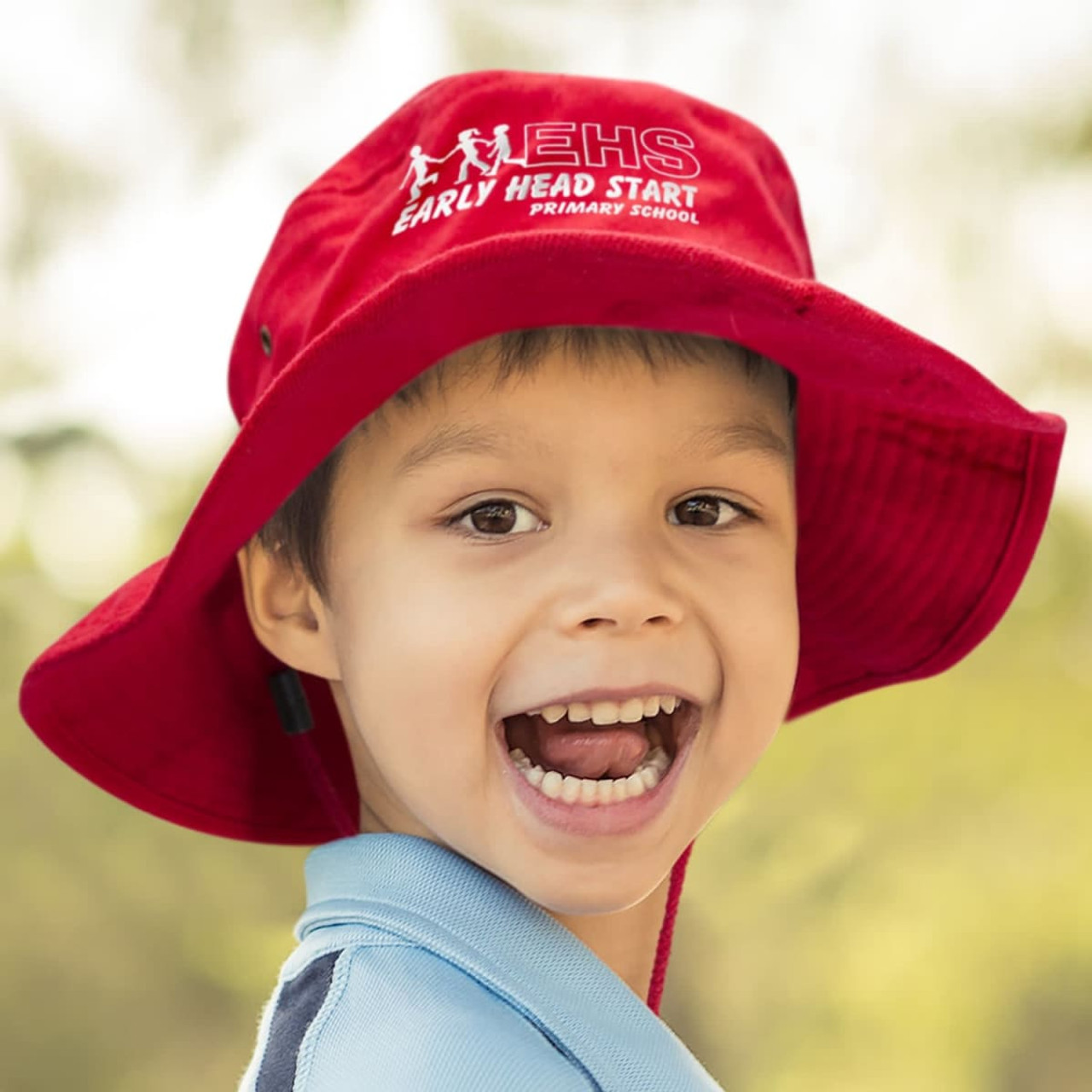 A wide-brimmed red hat with a logo, worn by a smiling child outdoors.