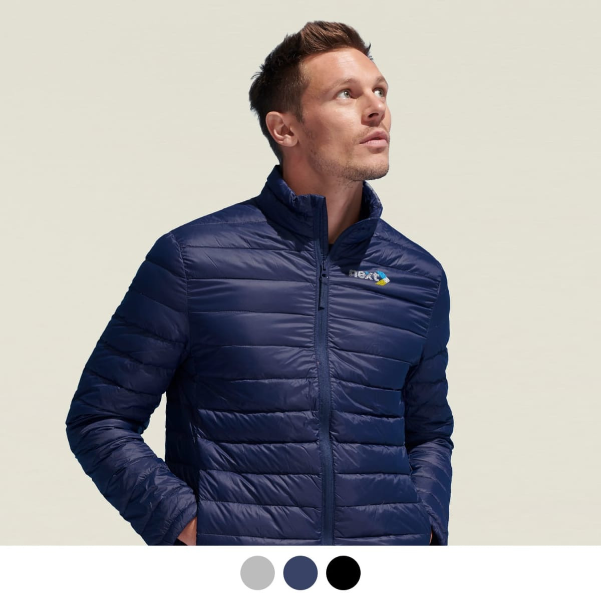 A man is wearing a navy blue puffer jacket, featuring a logo on the chest, against a light background.