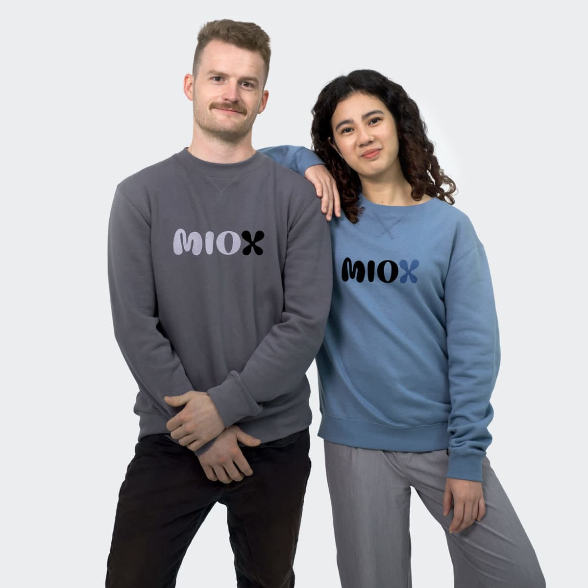 A grey unisex sweatshirt worn by a man and a blue unisex sweatshirt worn by a woman, both featuring a logo.