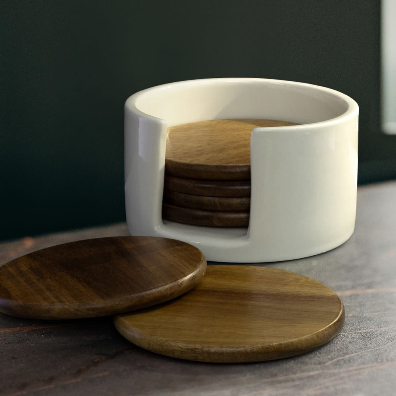 A white holder contains wooden coasters, with a few coasters resting on a dark surface.