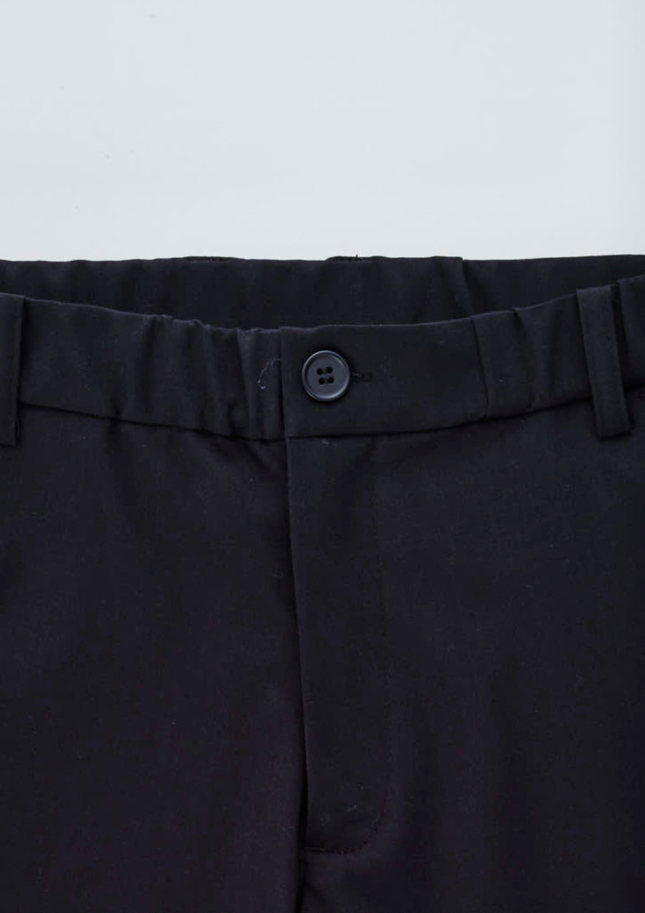 A close-up of black cargo pants featuring a button closure and elastic waistband. Logo present.