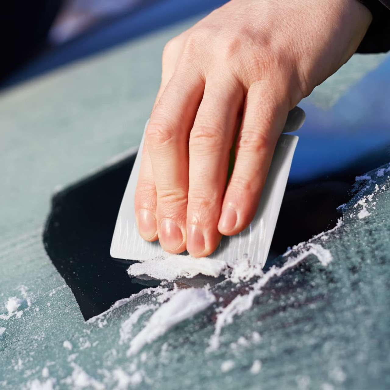 A compact ice scraper with a textured surface is being used to remove ice from a glass surface.