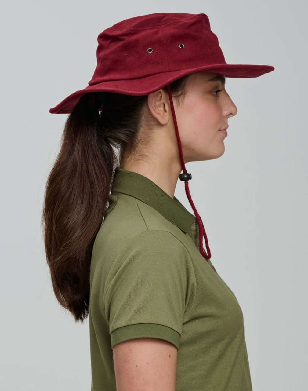 A maroon surf hat with a wide brim, featuring a chin strap and ventilation holes, worn by a person with long hair.