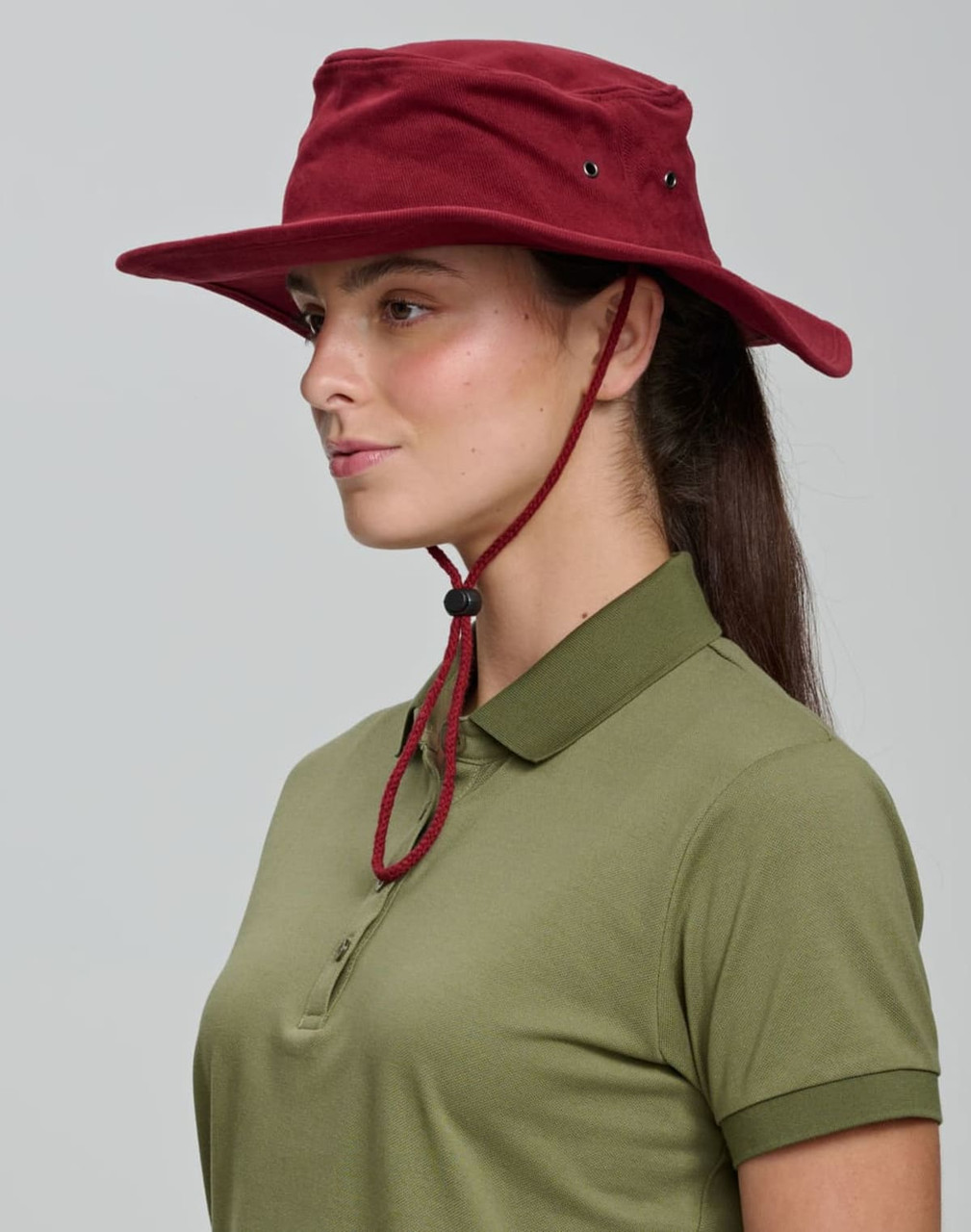 A burgundy bucket hat with a chin strap displayed on a person wearing a green polo shirt. Features a logo.