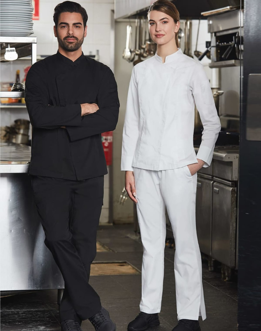 A black chef jacket and a white chef jacket worn by a man and a woman in a kitchen setting.