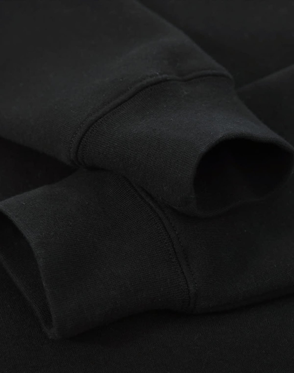 A black crew fleece jumper featuring ribbed cuffs, showcasing a soft fabric texture. It has a branding logo.