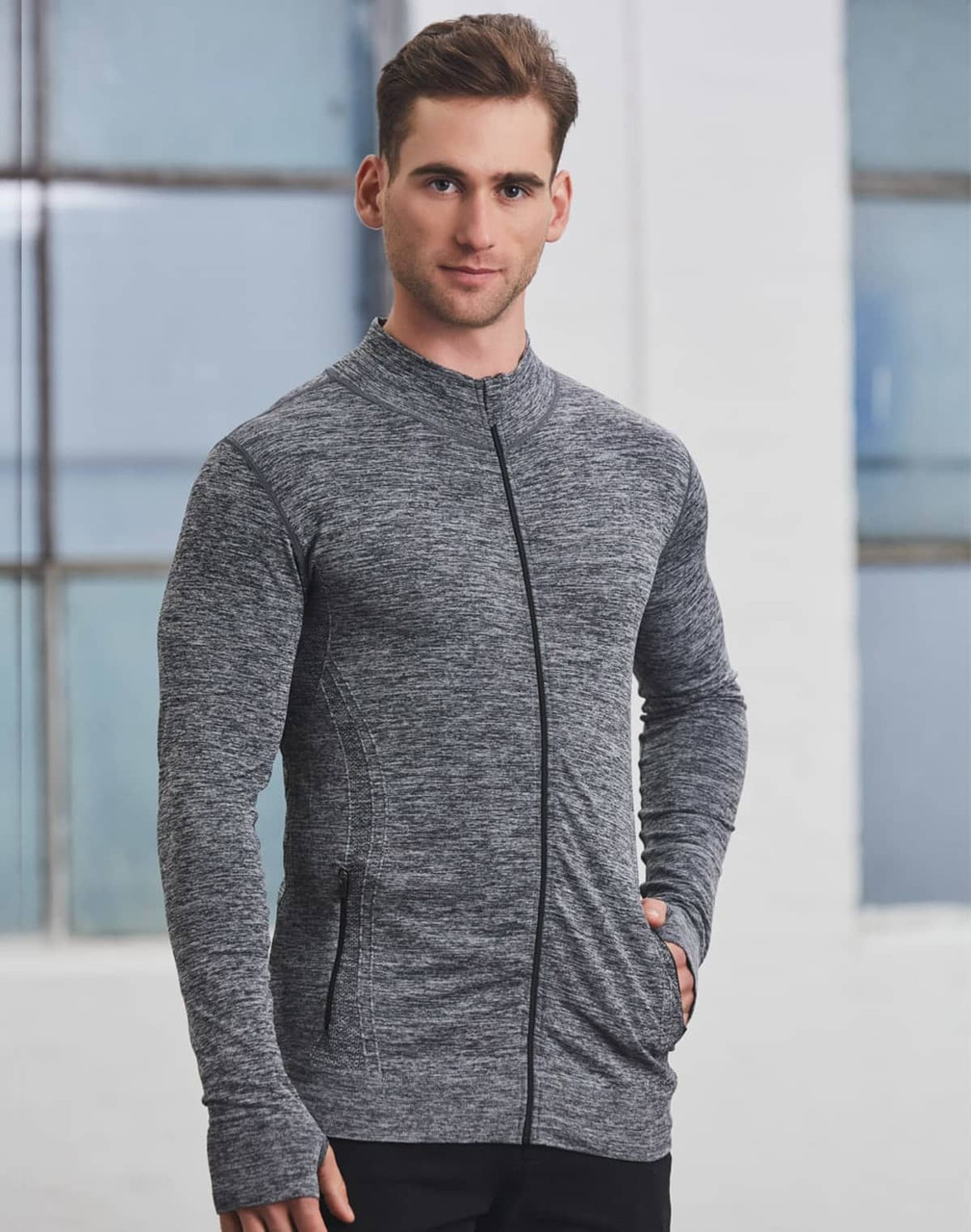 A man wearing a grey seamless jacket with a zip, featuring a fitted design and pockets.
