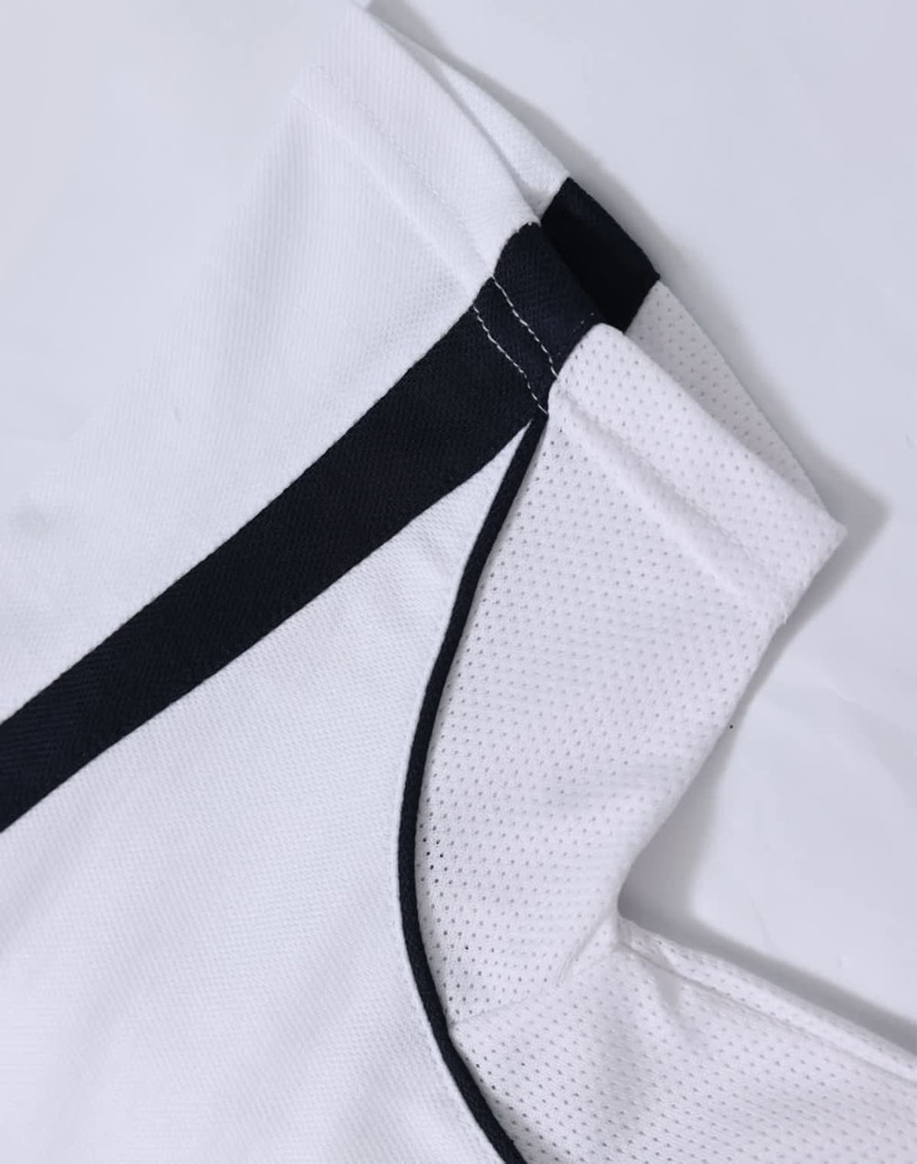 A white polo shirt with black accents, featuring a logo. The fabric has a textured, breathable appearance.