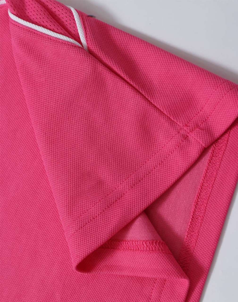 A close-up of a pink polo shirt featuring short sleeves and contrasting trim. The shirt includes a logo.