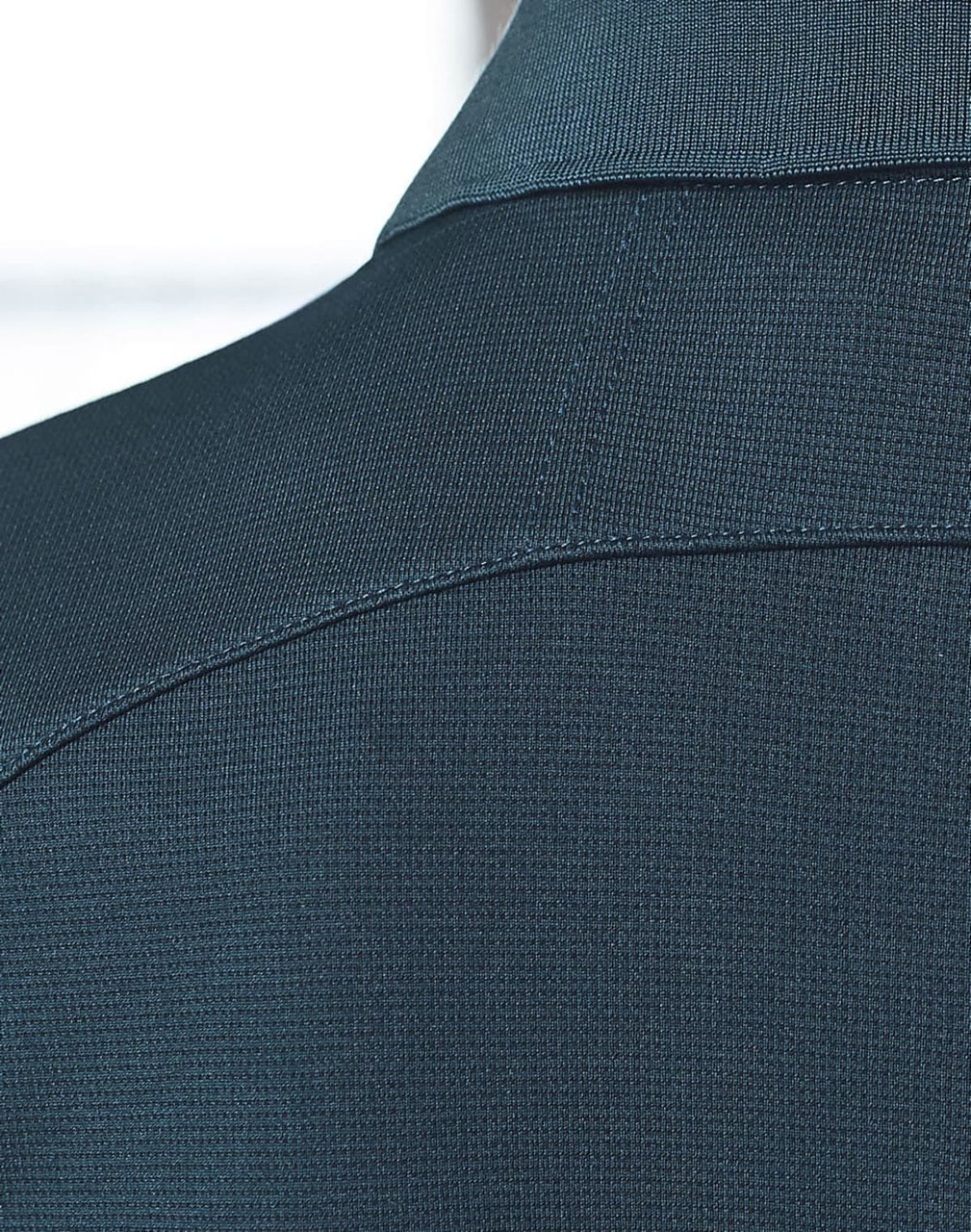 A close-up of a dark green polo shirt, featuring a textured fabric and a collar. The shirt has a logo present.