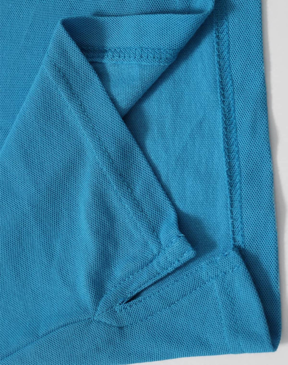 A close-up of a turquoise polo shirt featuring a fold at the sleeve and a branding logo.