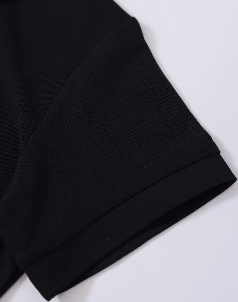 A close-up of a black polo shirt sleeve featuring a folded cuff and a subtle branding logo.