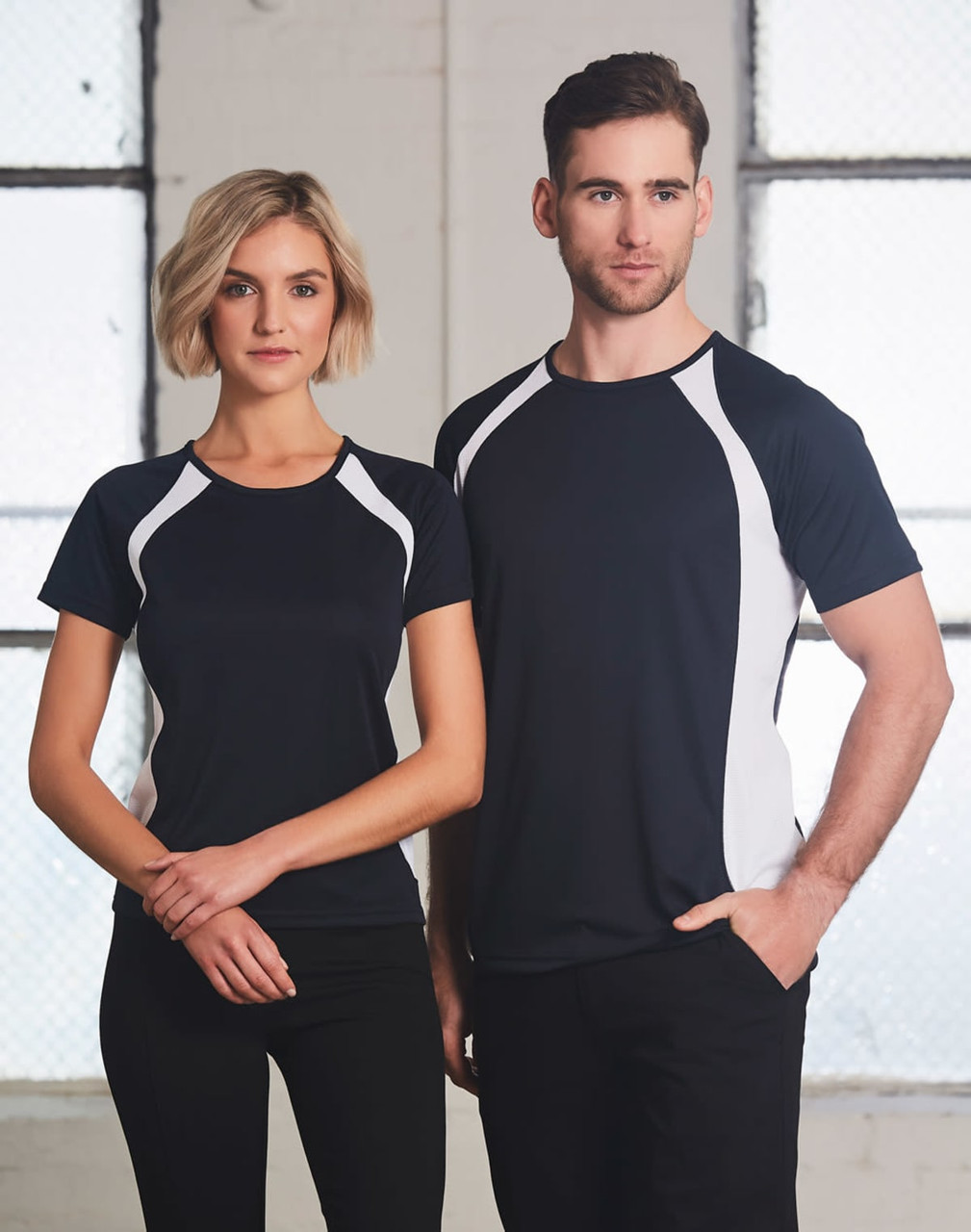 A pair of models wearing a black and white men's premier tee shirt. The shirt features contrasting side panels and a logo.