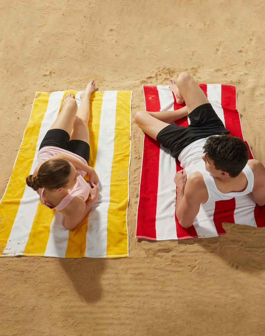 Striped beach towels in yellow and red, laid out on sand, with a man and woman relaxing on them.