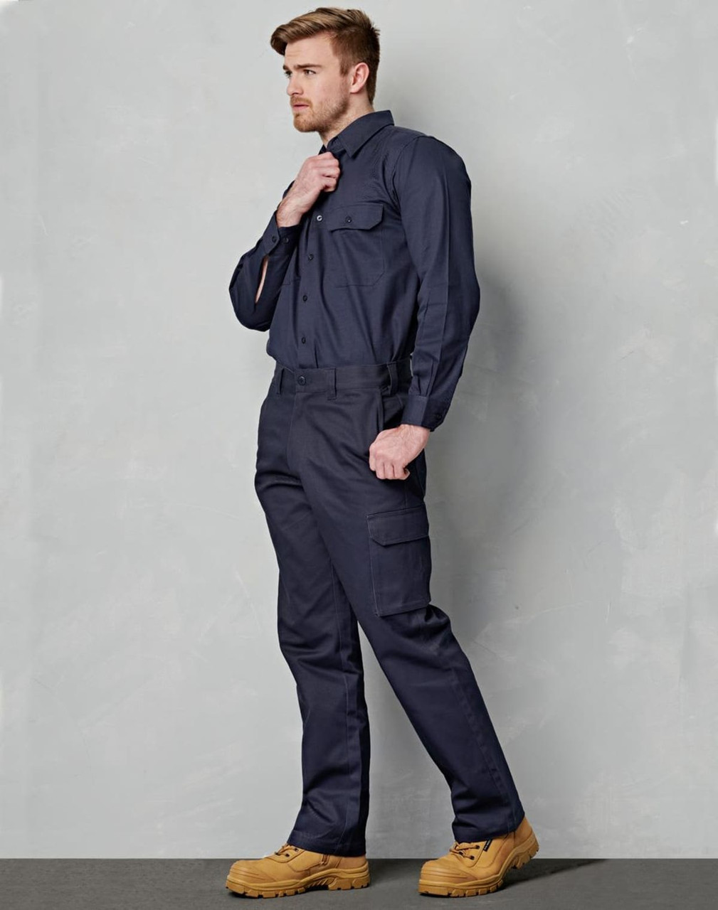 A man wearing navy cargo pants with a drill pant pocket on the leg, paired with a matching shirt and work boots.