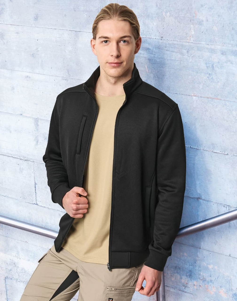 A man wearing a black jacquard fleece jacket over a beige shirt, set against a blue background. The jacket features a logo.