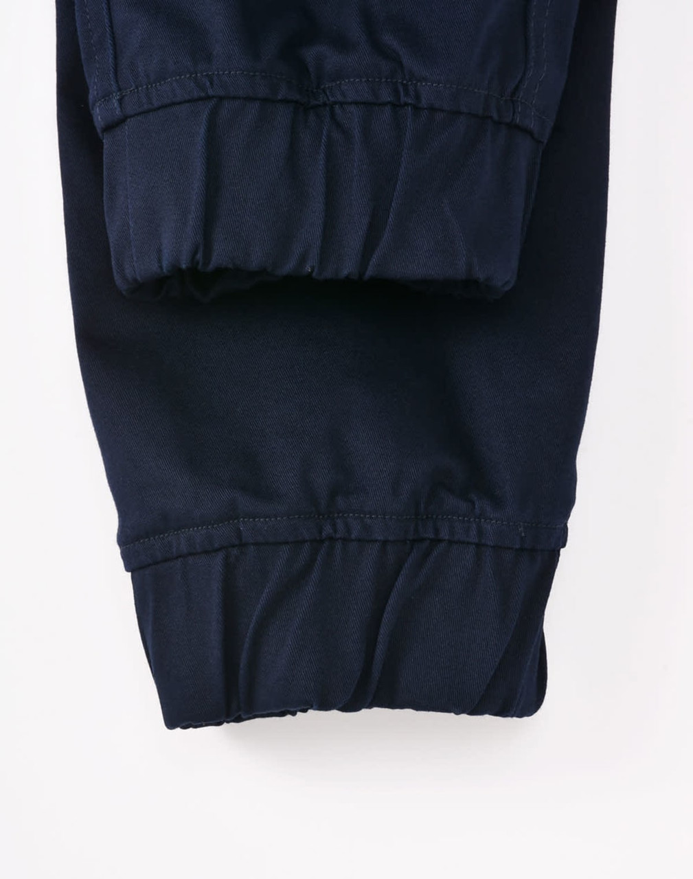 A pair of navy unisex cotton stretch drill cuffed work pants with gathered cuffs. Features a logo on the waistband.