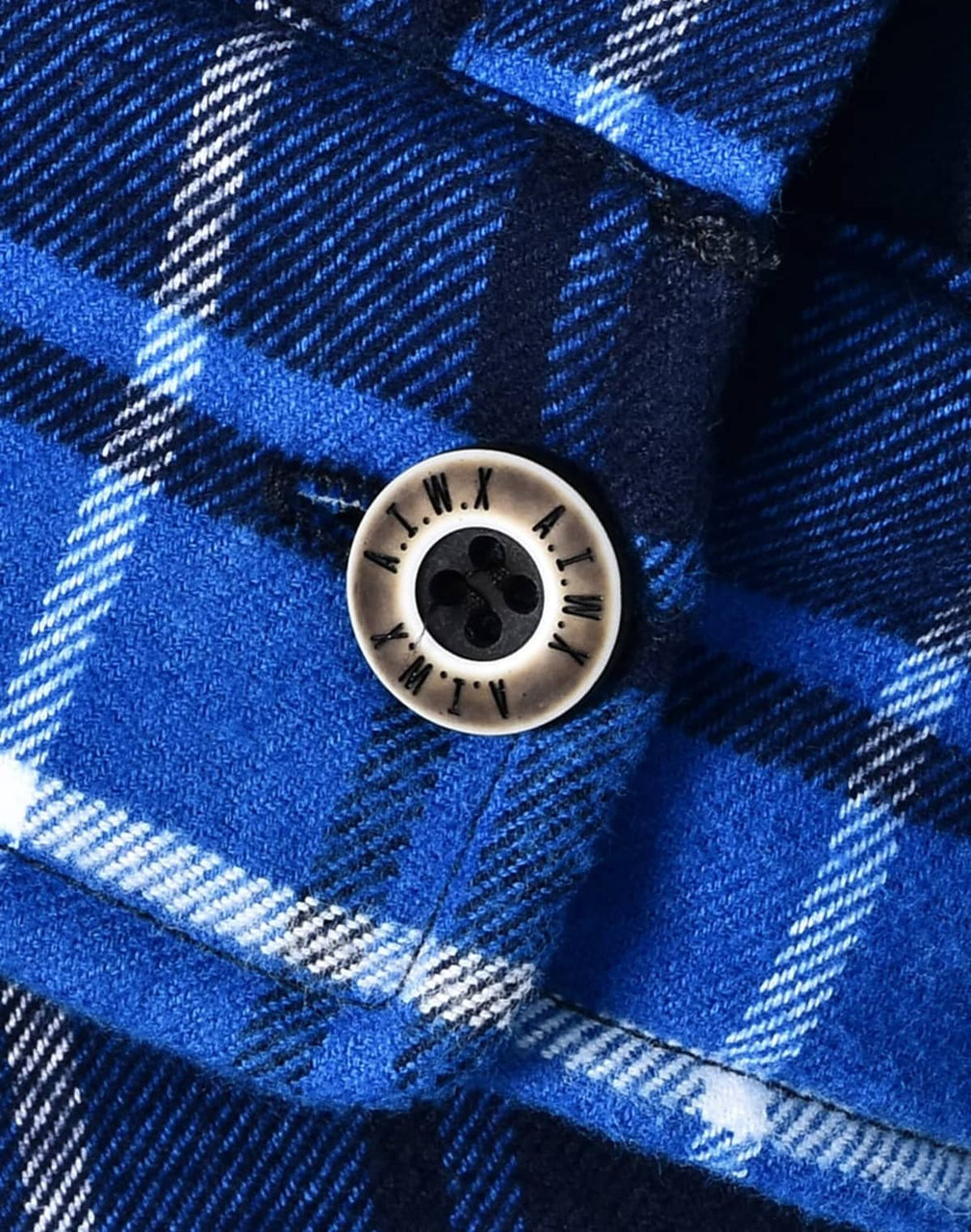 A close-up of a blue and white checkered flannel shirt featuring a round button and a logo.