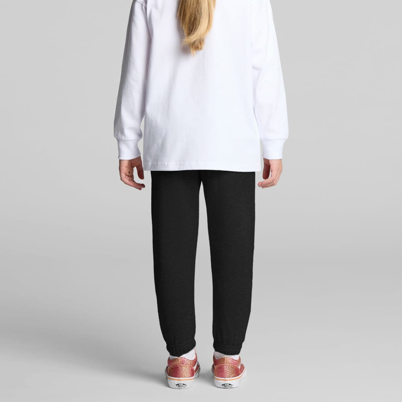 Black track pants for kids, featuring a tapered fit and cuffed ankles, paired with a white long-sleeve top.