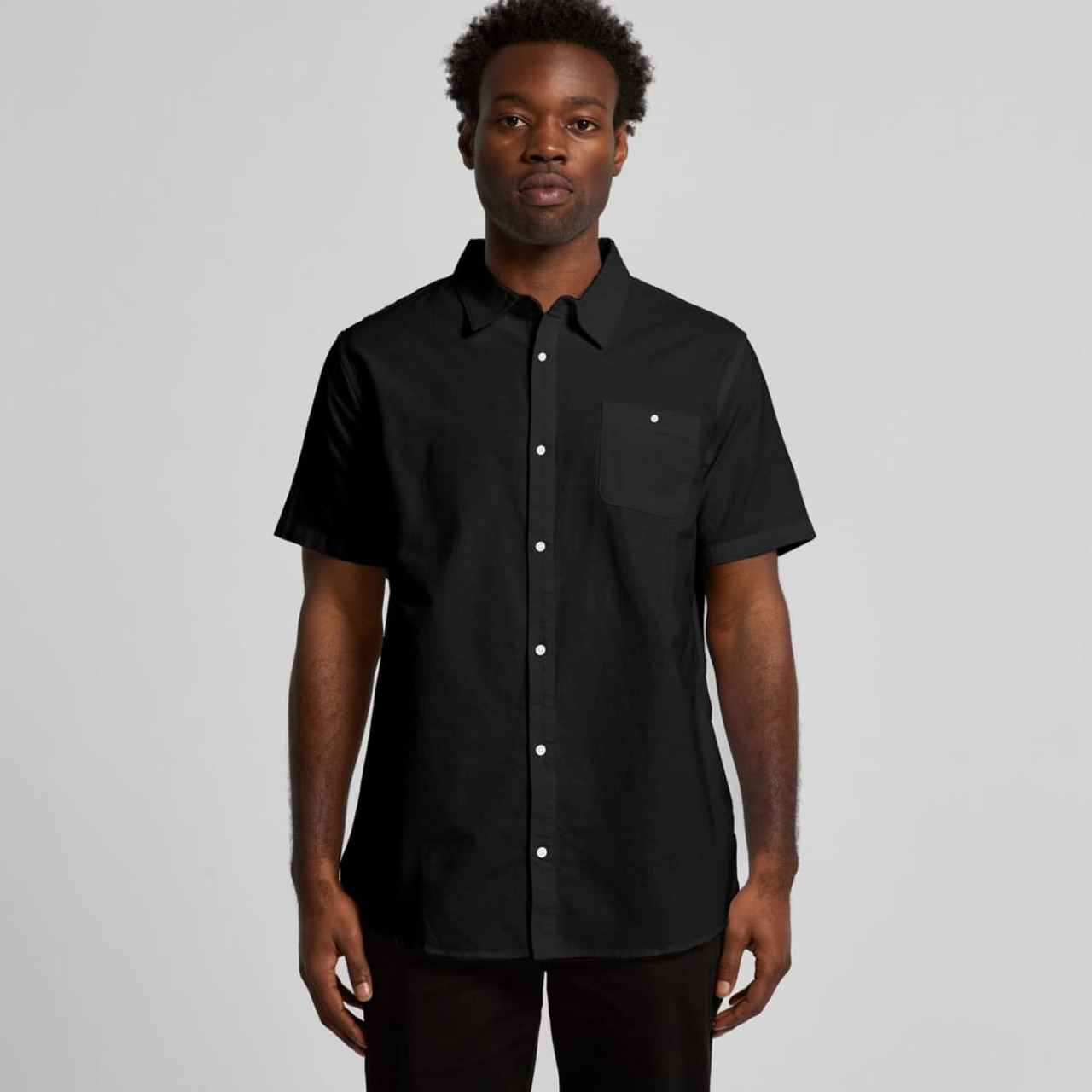 A black short-sleeved button-up shirt with a pocket. The model is wearing it against a plain background.