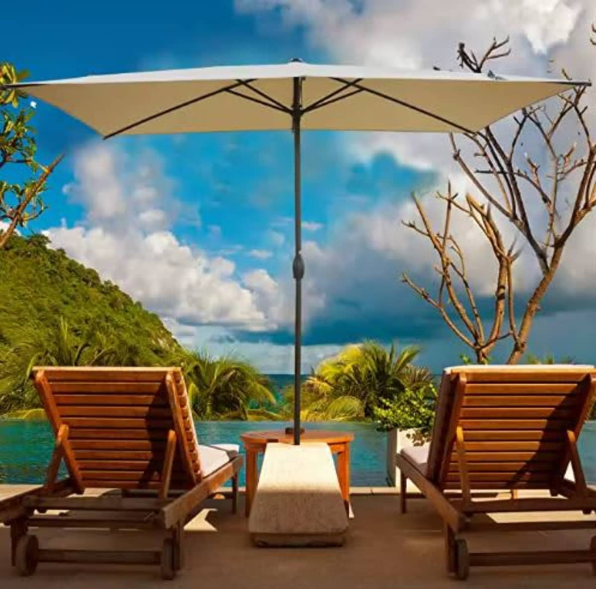 A market umbrella in white stands between two wooden lounge chairs, set against a tropical landscape and blue sky.