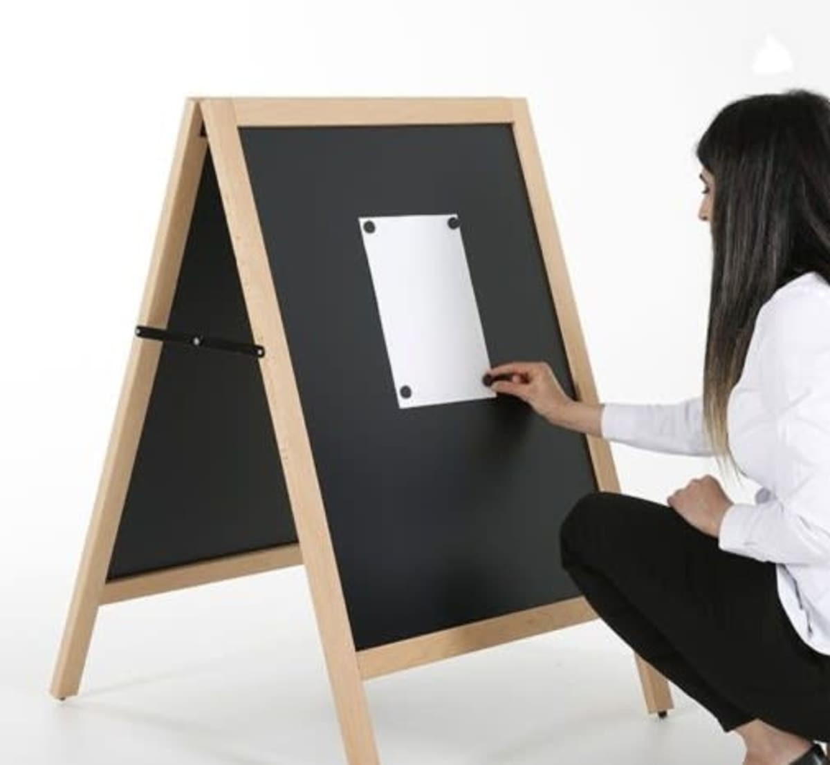 A magnetic black chalkboard A-frame with a wooden frame, being used by a person to attach a note.
