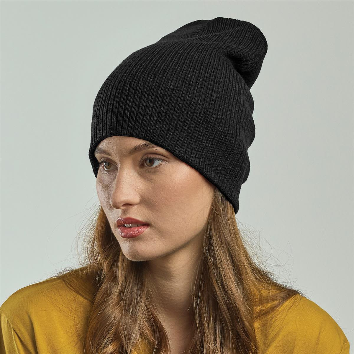 A black ribbed beanie is worn by a model with long hair, styled casually against a neutral background.