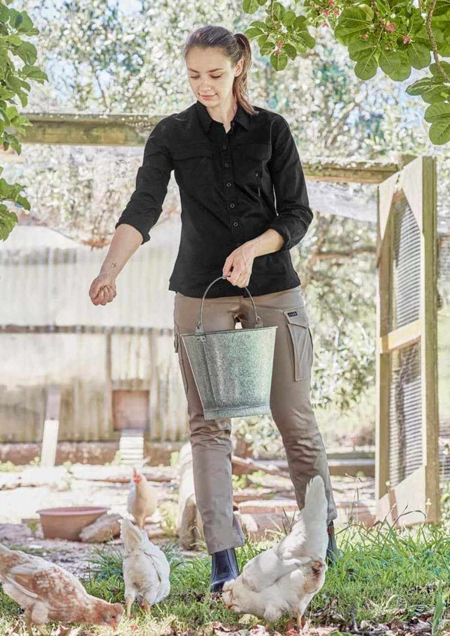 A woman wearing a black long sleeve shirt and khaki pants, engaging with chickens while holding a bucket.