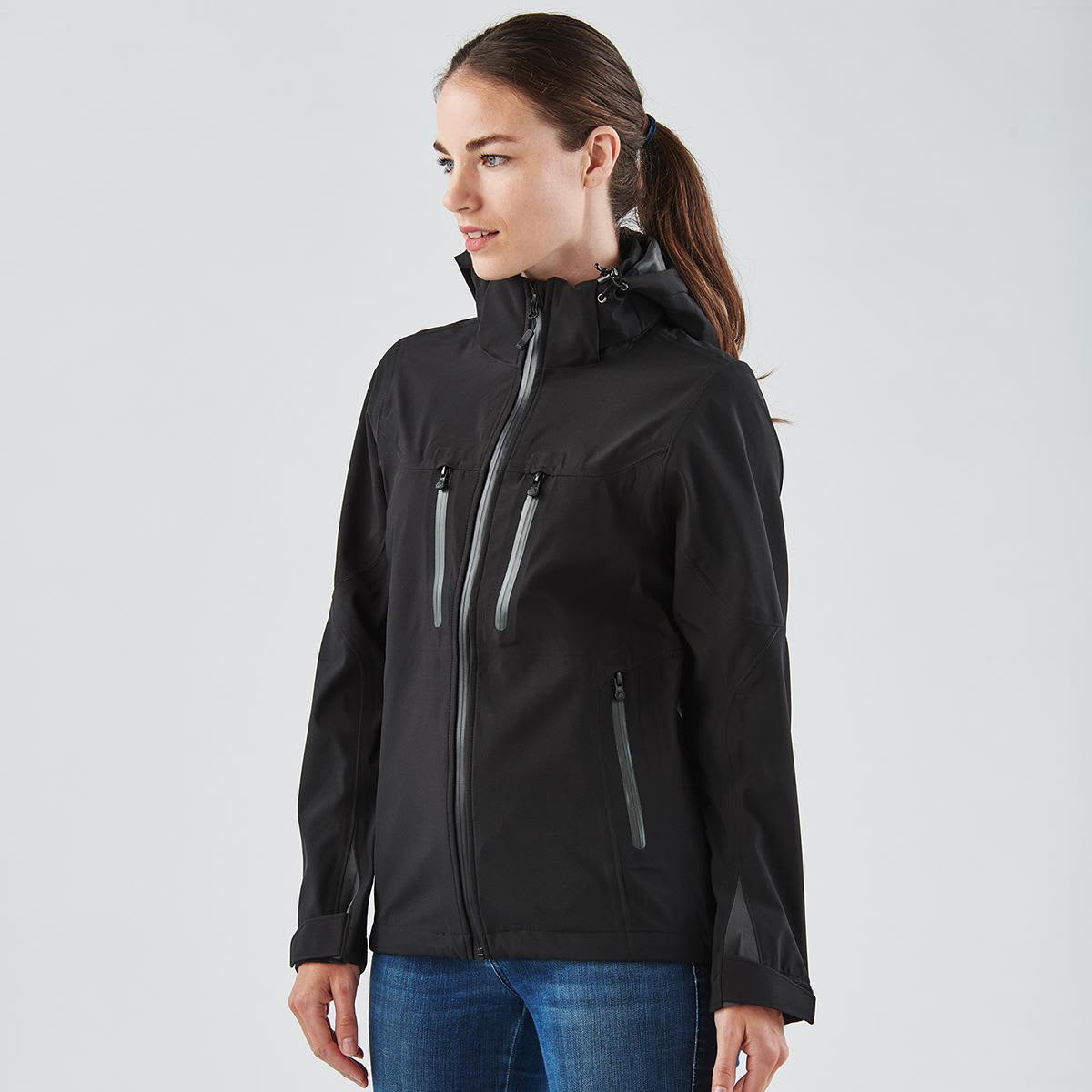A black women's softshell jacket featuring zippered pockets and a hood, with subtle reflective accents.