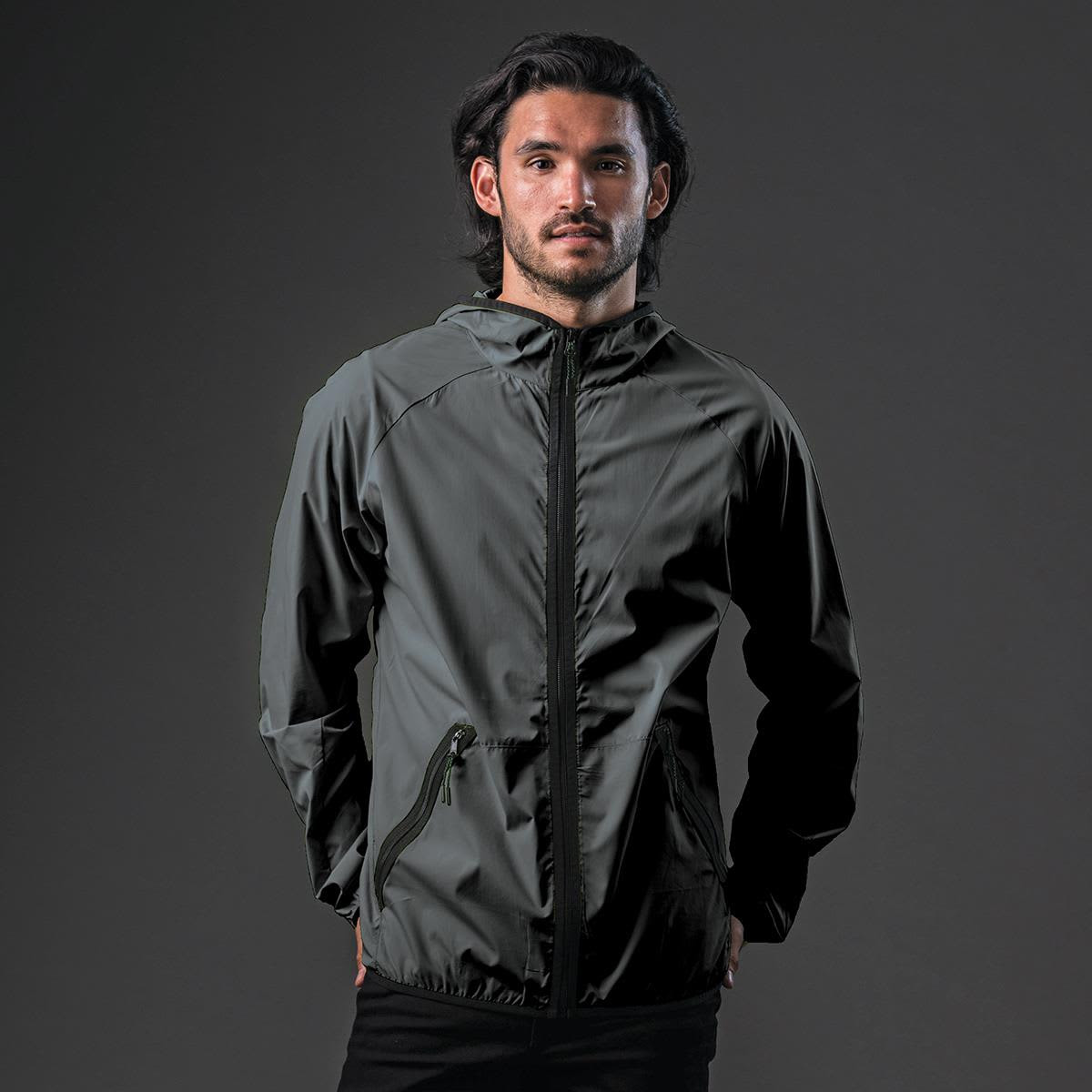 A man wearing a dark grey hooded rain jacket with a zip and a logo on the chest.