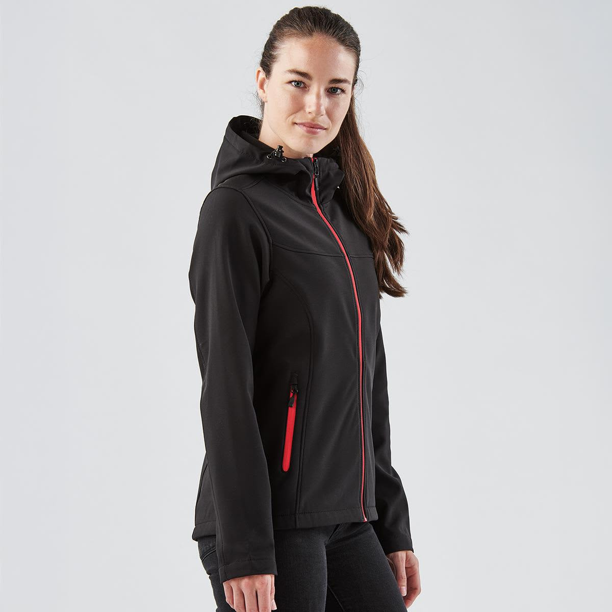 A black softshell hoody with a red zipper and accents, featuring a hood and zippered pockets, displayed on a model.