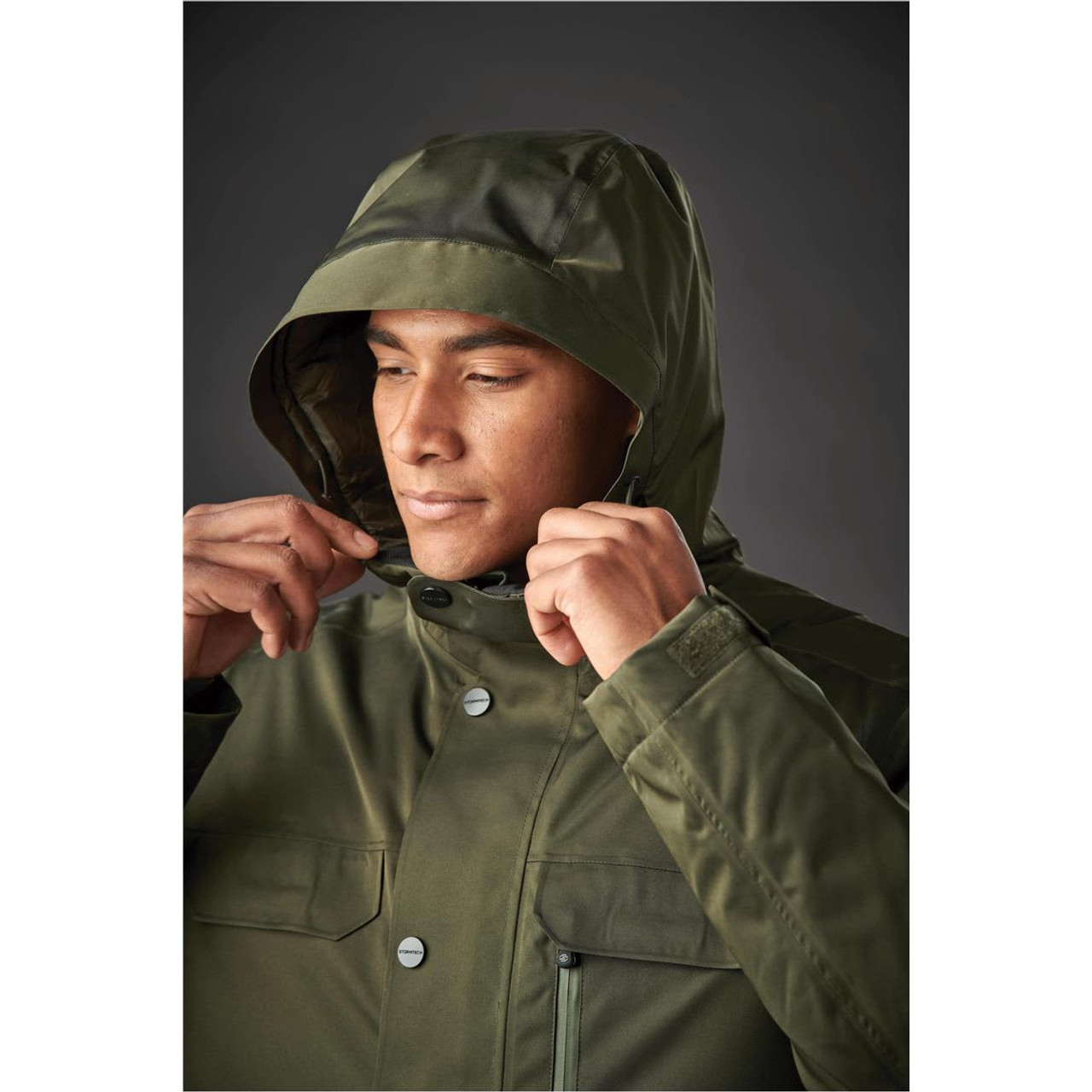 A man in a dark green thermal jacket with a hood and front pockets, featuring a logo.