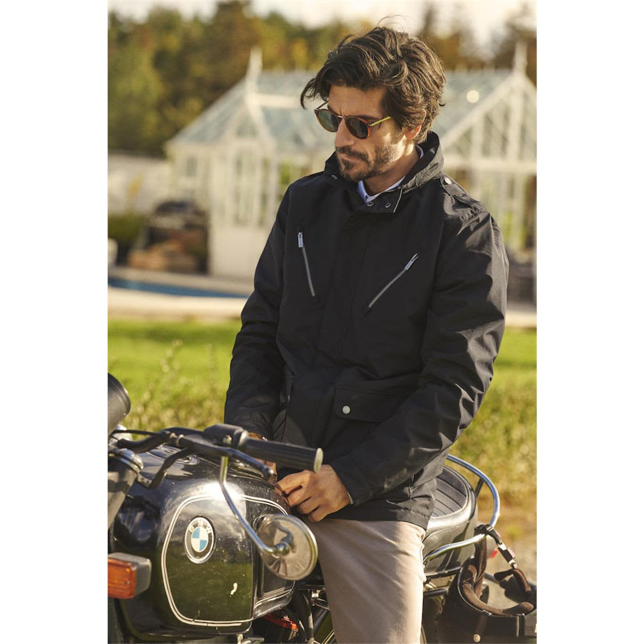 A black men's business coat with zippered pockets, worn by a man next to a motorcycle in an outdoor setting.