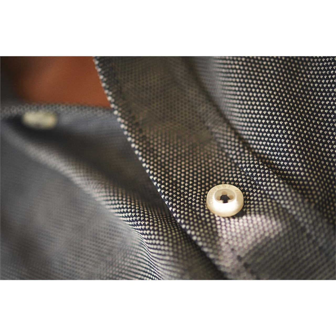 A close-up of a grey button-up shirt featuring a textured fabric and a white button. The shirt has a branding logo.