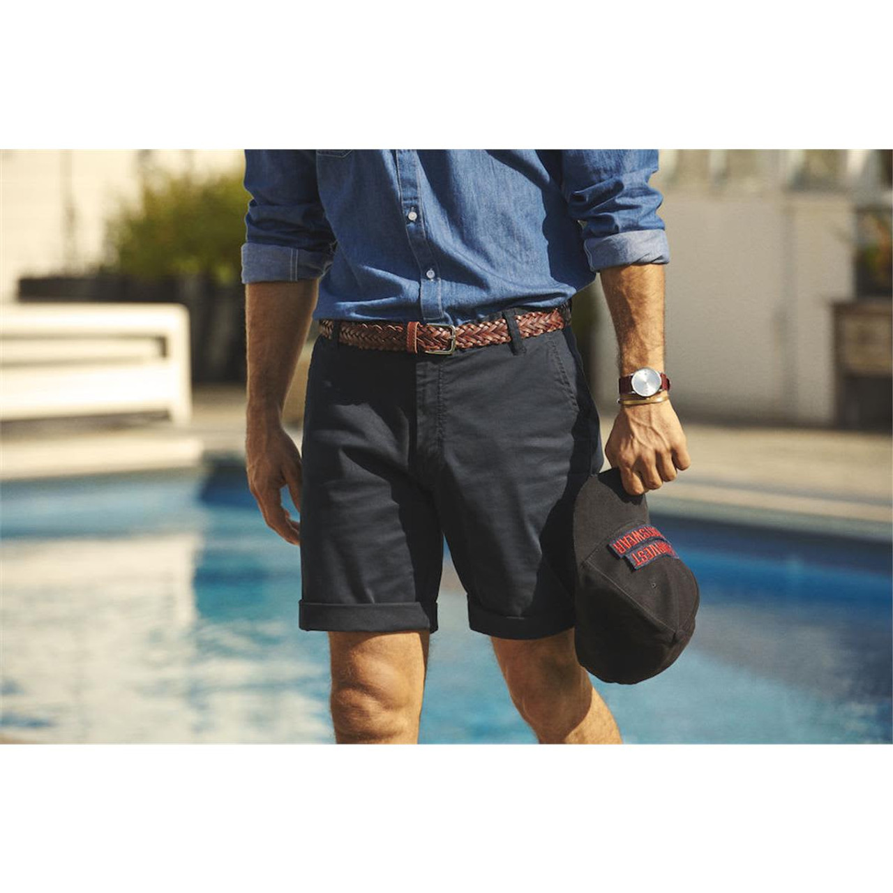 Men's dress shorts in navy, featuring rolled hems and a patterned belt, paired with a casual shirt and cap.