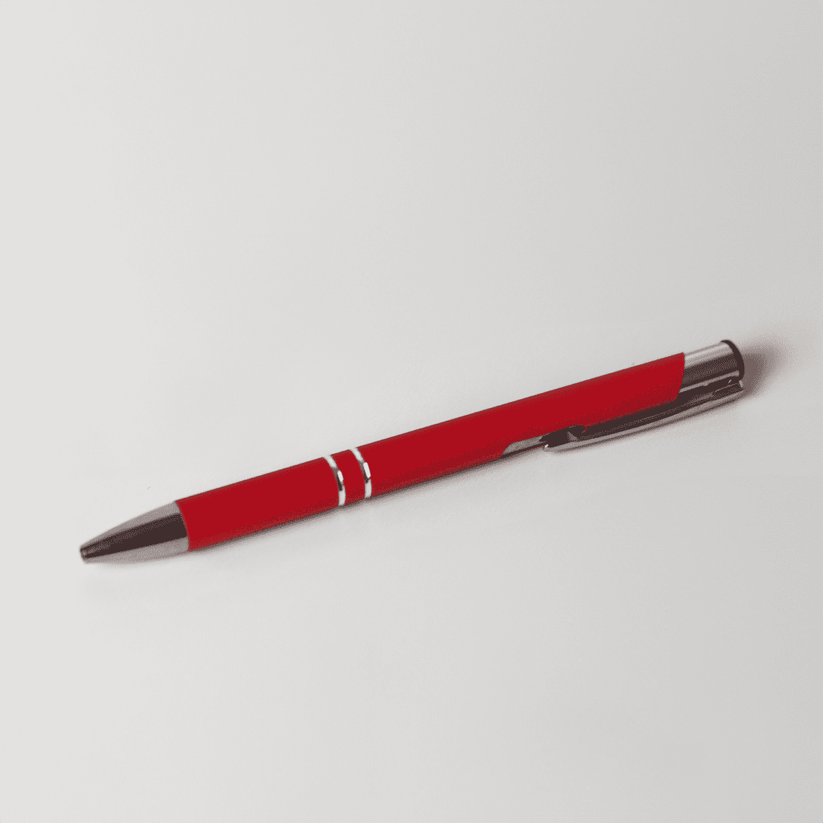 A red metal pen with a shiny silver clip, featuring two decorative silver bands.