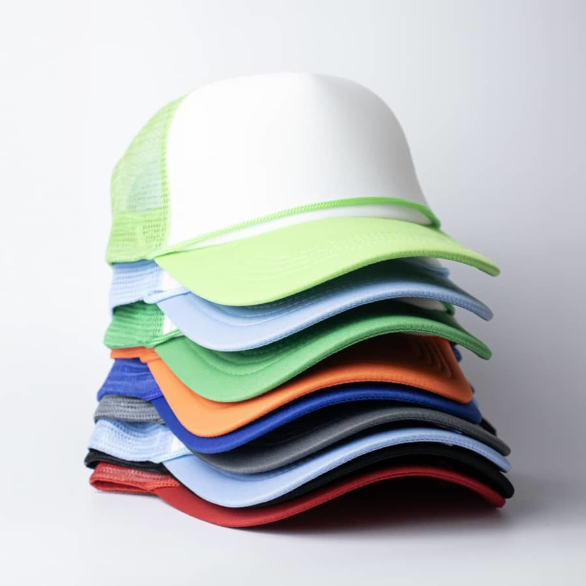 A stack of vibrant trucker caps in various colours, featuring mesh backs and curved visors, with a logo present.
