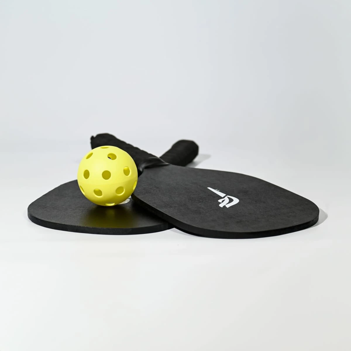 A black pickleball set featuring two paddles and a yellow ball, with a logo on the paddles.