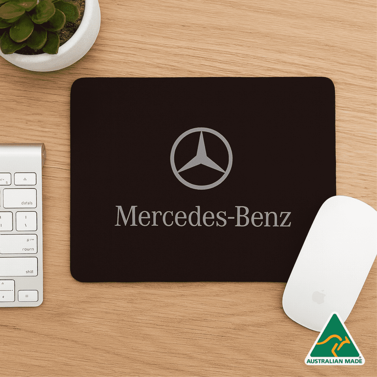 A black mouse mat featuring a logo and text, set on a wooden desk alongside a keyboard and a mouse.