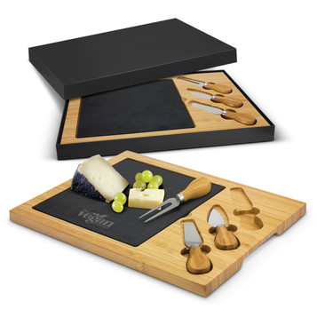A slate cheese board with bamboo accents and cheese knives, presented in a black box, featuring a logo. A slate cheese board with bamboo accents and cheese knives, presented in a black box, featuring a logo.