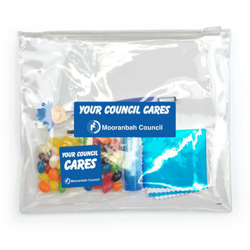 A clear pouch containing colorful candies, a lip balm, a small blue package, and a cleaning cloth, with branding visible.